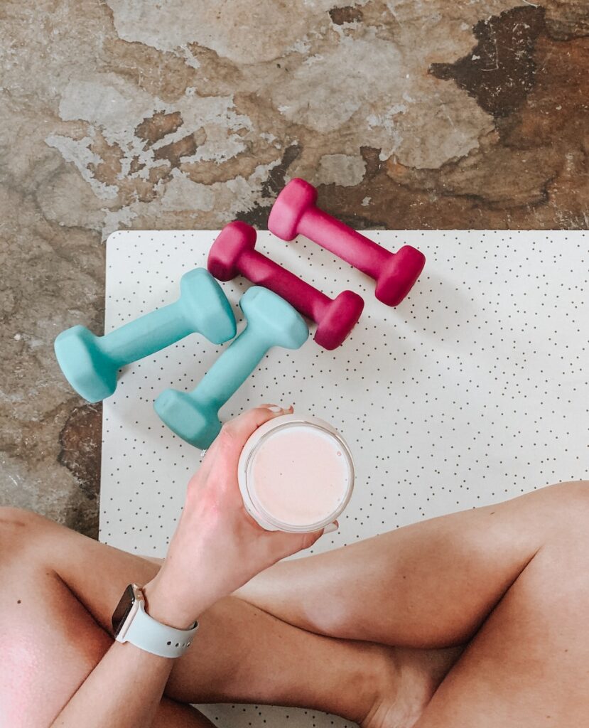 person holding white liquid filled cup above two pairs of dumbbells