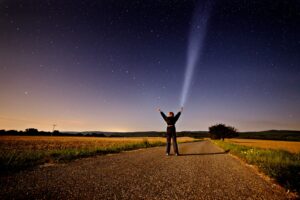 person raising his two hands while holding flashlight standing on road between grass during sunset